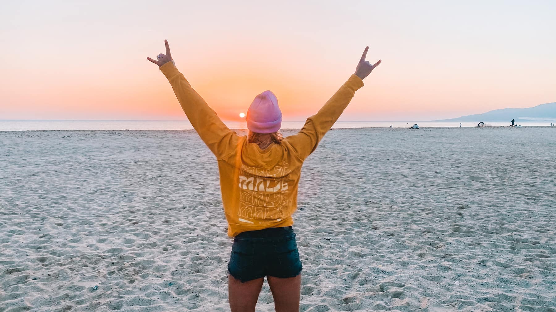 Woman standing on Tarifa beach at sunset with arms raised