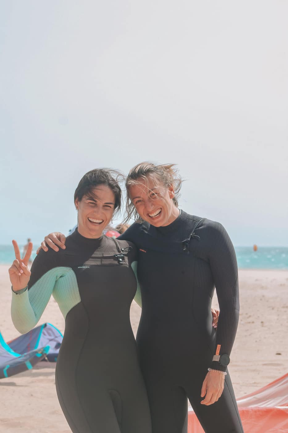 Two women smiling together in wetsuits on the beach