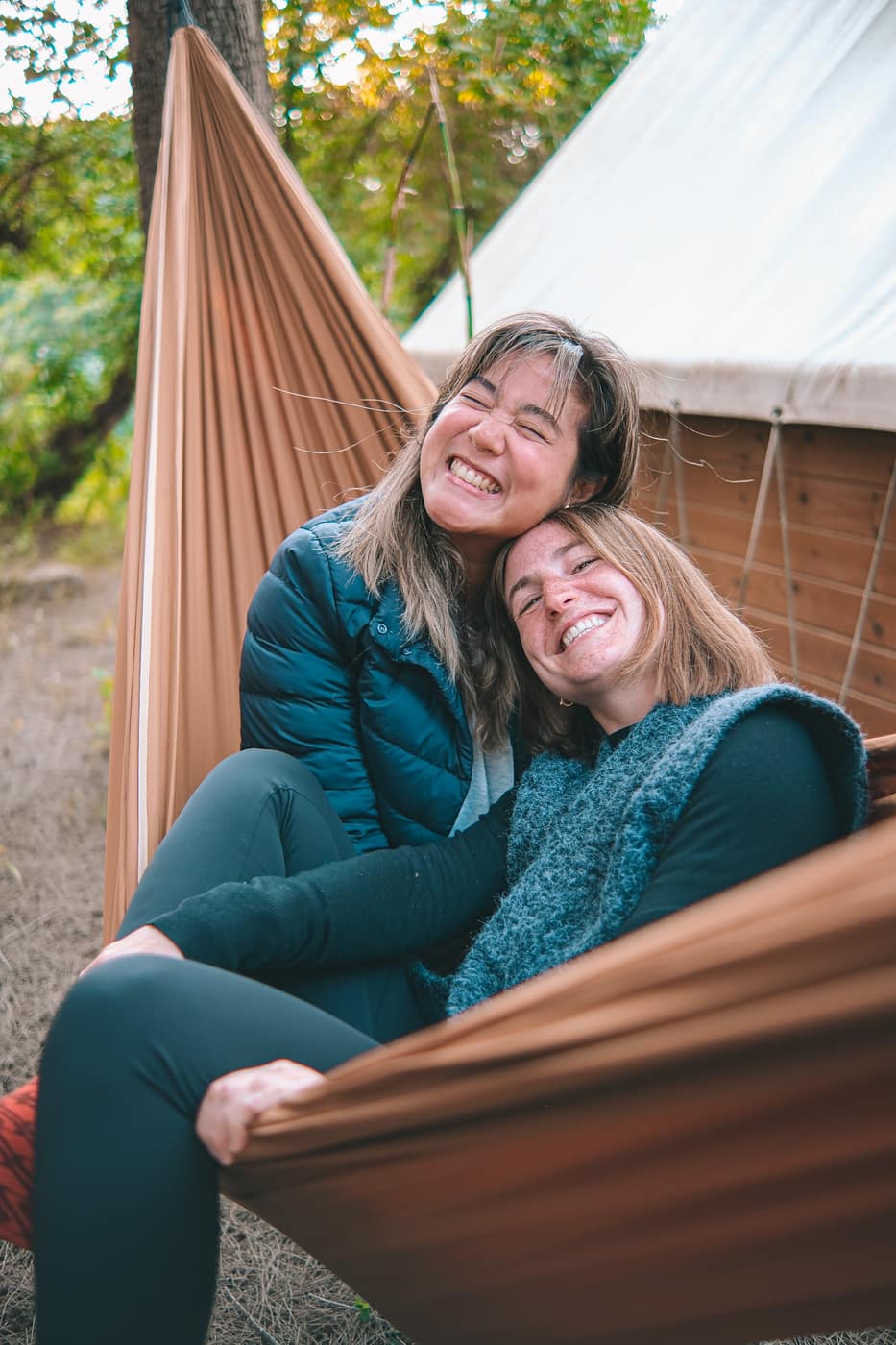 Two women smiling together in a hammock at camp